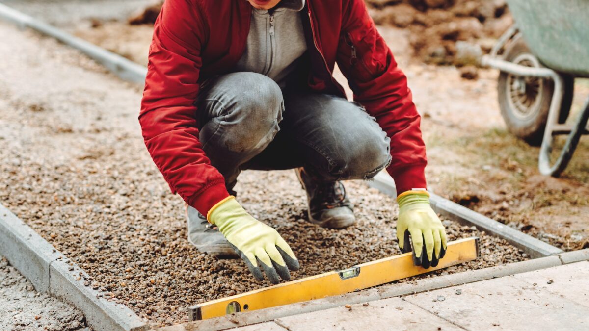 Close up of construction worker installing and laying pavement stones. Worker using slabs and level to build deck