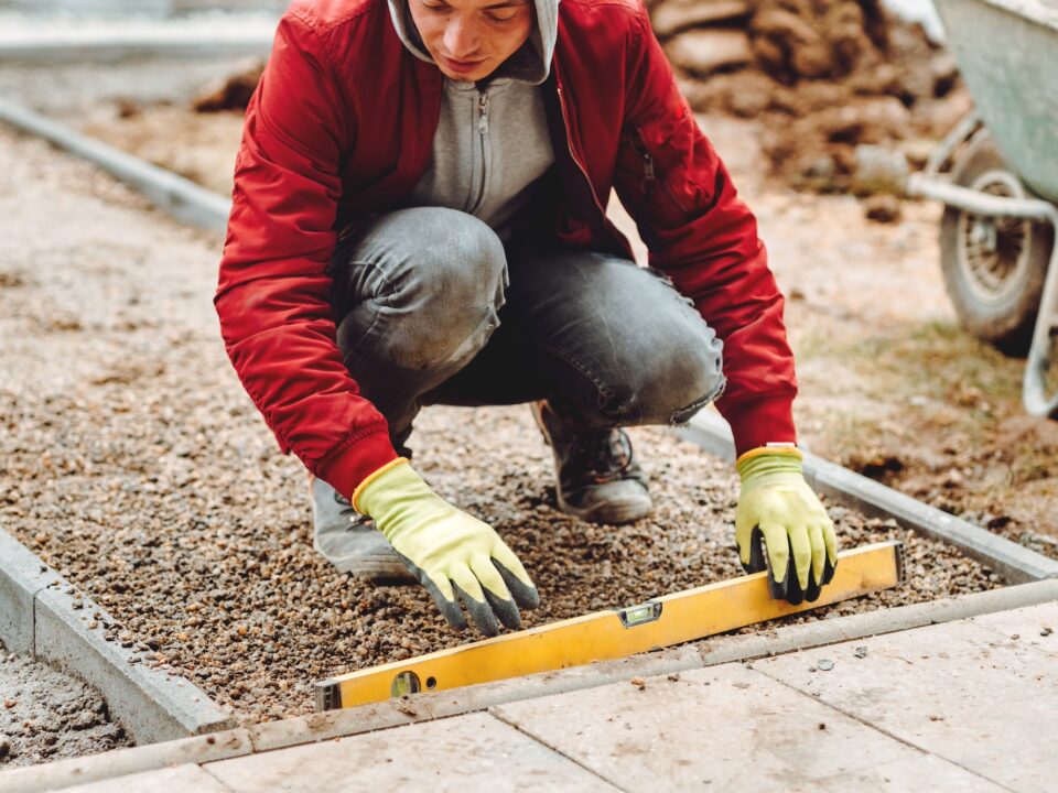 Close up of construction worker installing and laying pavement stones. Worker using slabs and level to build deck