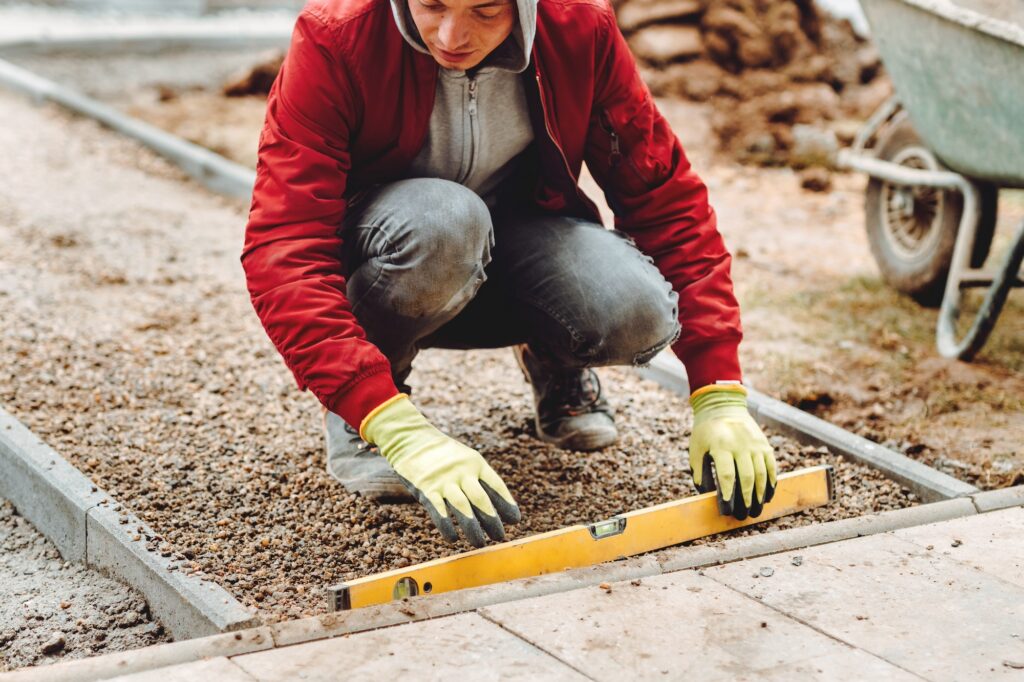Close up of construction worker installing and laying pavement stones. Worker using slabs and level to build deck