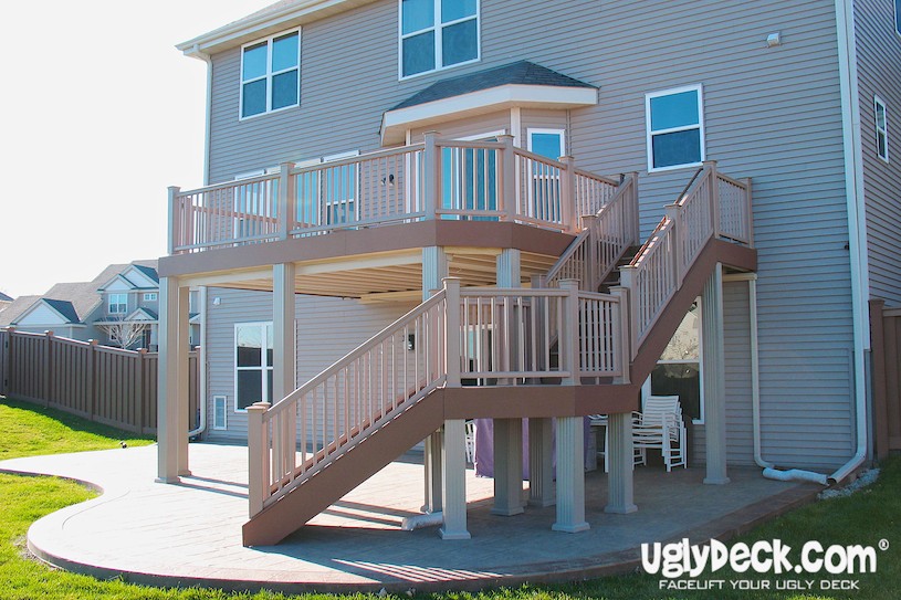A two-story beige house with a large, elevated wooden deck installed by a professional Deck Builder. Featuring stairs, railings, and a covered patio beneath, the deck overlooks a fenced backyard with green grass. “uglydeck.com” is visible in the corner.
