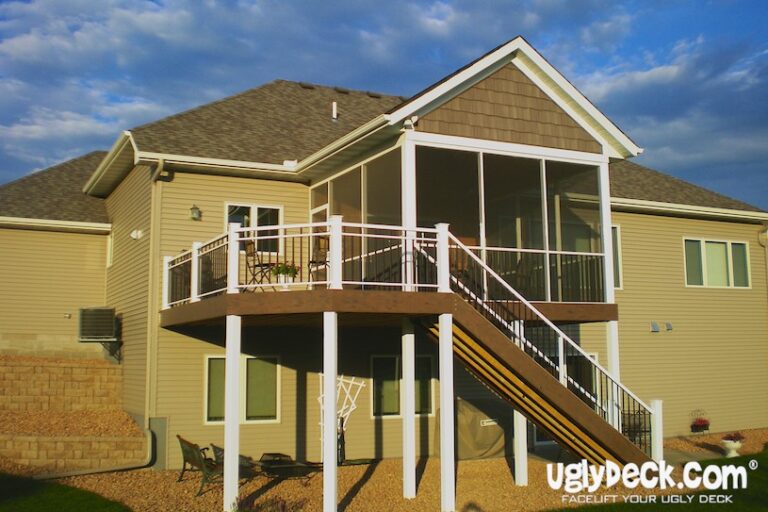 A two-story house with beige siding features a screened-in deck, crafted by a professional Deck Builder, with white railings and a staircase leading to the landscaped backyard. uglydeck.com is visible in the bottom right corner.