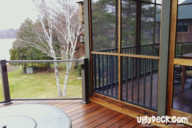 A backyard deck with wooden flooring, glass and black metal railing, and a screened-in porch area—perfect for those seeking DIY deck materials or a trusted deck builder. Grass, trees, and a lake are visible. The UglyDeck.com logo appears in the corner.