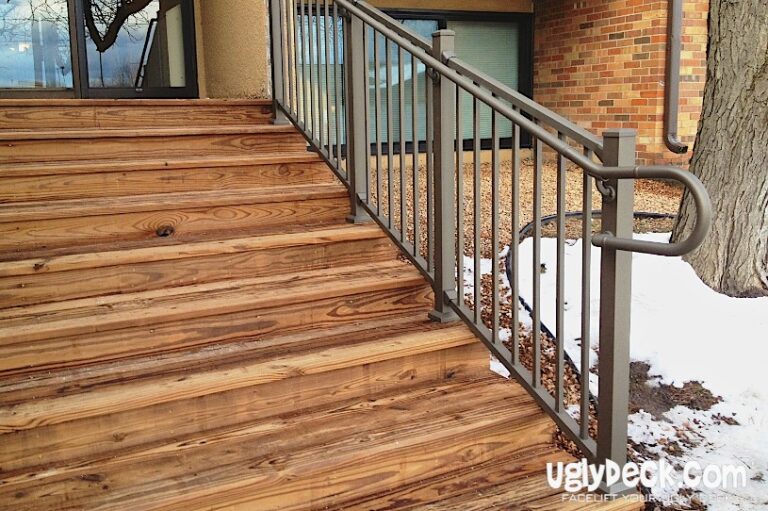 Wooden outdoor stairs with a metal railing beside a building, crafted using quality DIY deck materials. Snow covers the ground near the stairs and tree, highlighting signs of weathering. The uglydeck.com logo is visible in the bottom right corner.