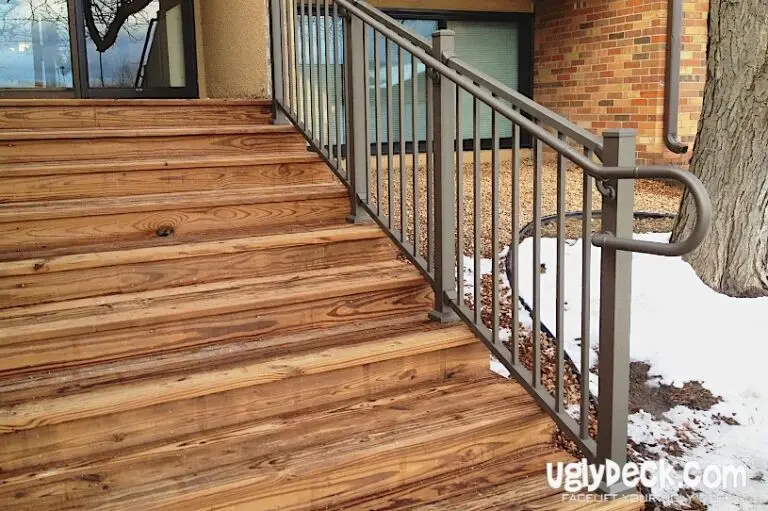 Wooden outdoor stairs with a metal railing beside a building, crafted using quality DIY deck materials. Snow covers the ground near the stairs and tree, highlighting signs of weathering. The uglydeck.com logo is visible in the bottom right corner.