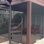 A screened-in patio features outdoor seating beneath an elevated deck crafted with quality DIY Deck Materials, accessible by a metal spiral staircase and surrounded by a landscaped yard.