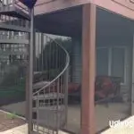 A screened-in patio features outdoor seating beneath an elevated deck crafted with quality DIY Deck Materials, accessible by a metal spiral staircase and surrounded by a landscaped yard.