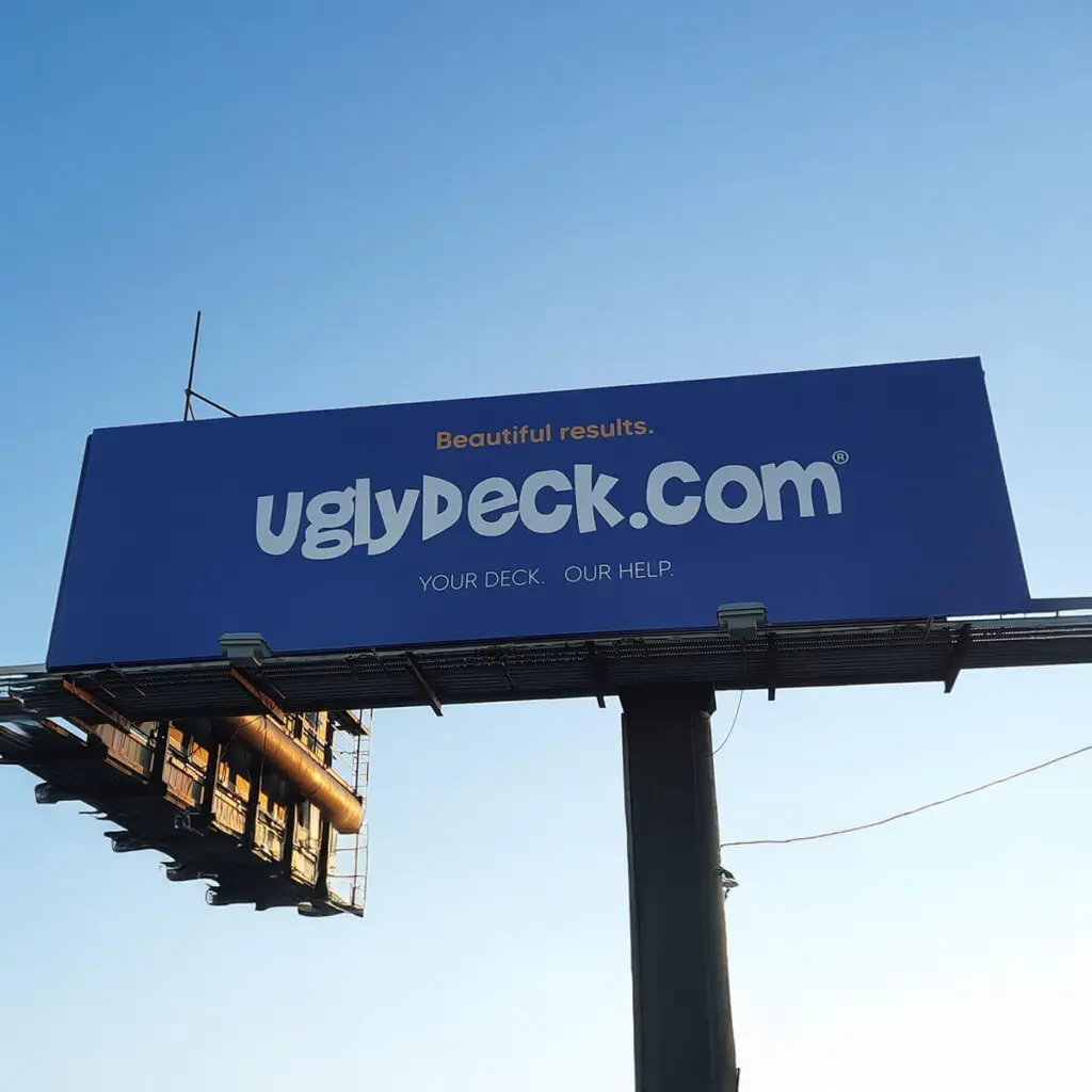 A large blue billboard reads Beautiful results. uglydeck.com® YOUR DECK. OUR HELP. DIY Deck Materials and expert Deck Install against a clear sky background.